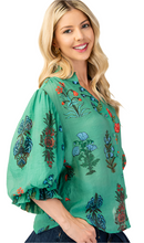 Load image into Gallery viewer, Woman wearing a green embroidered blouse with floral patterns on a beige background