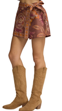 Load image into Gallery viewer, A close-up of a person wearing a brown patterned wrap-style mini skirt with orange and pink floral motifs, paired with tan cowboy boots, against a light gray studio background.