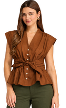 Load image into Gallery viewer, A woman modeling a brown sleeveless peplum blouse with a V-neck, button-front detail, and a self-tie waist sash, paired with dark green pants against a plain white background.